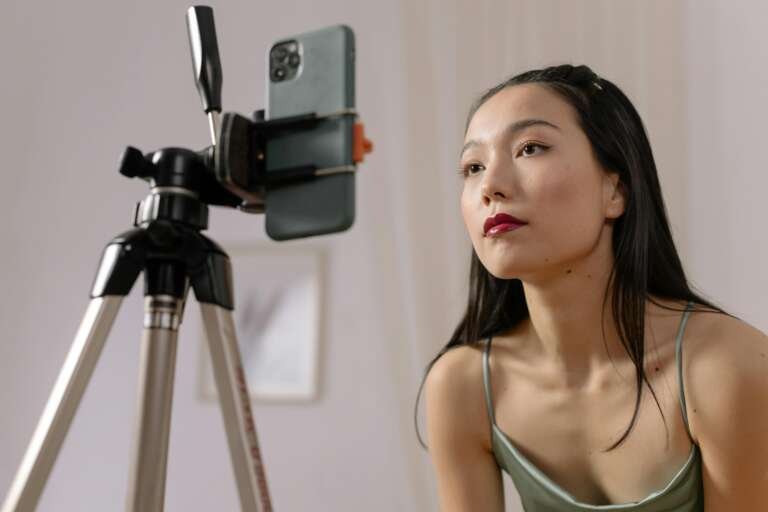 Asian woman recording a vlog indoors using a smartphone on a tripod.