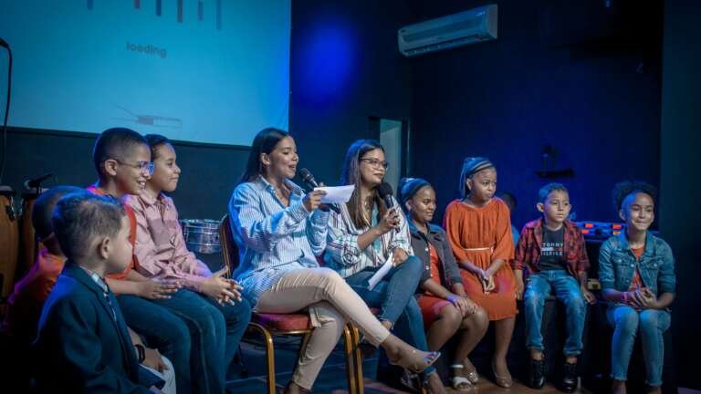 A group of children and young women participating in a panel discussion indoors.
