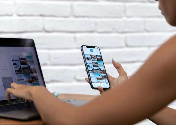 A woman working remotely using a laptop and smartphone, focusing on social media content.